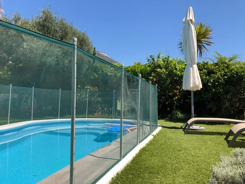 A removable mesh pool safety fence installed around a backyard swimming pool.